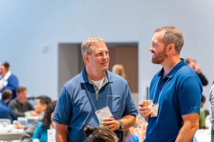 Attendees standing during the July HMS meeting, engaged in discussion and collaboration in a professional setting.