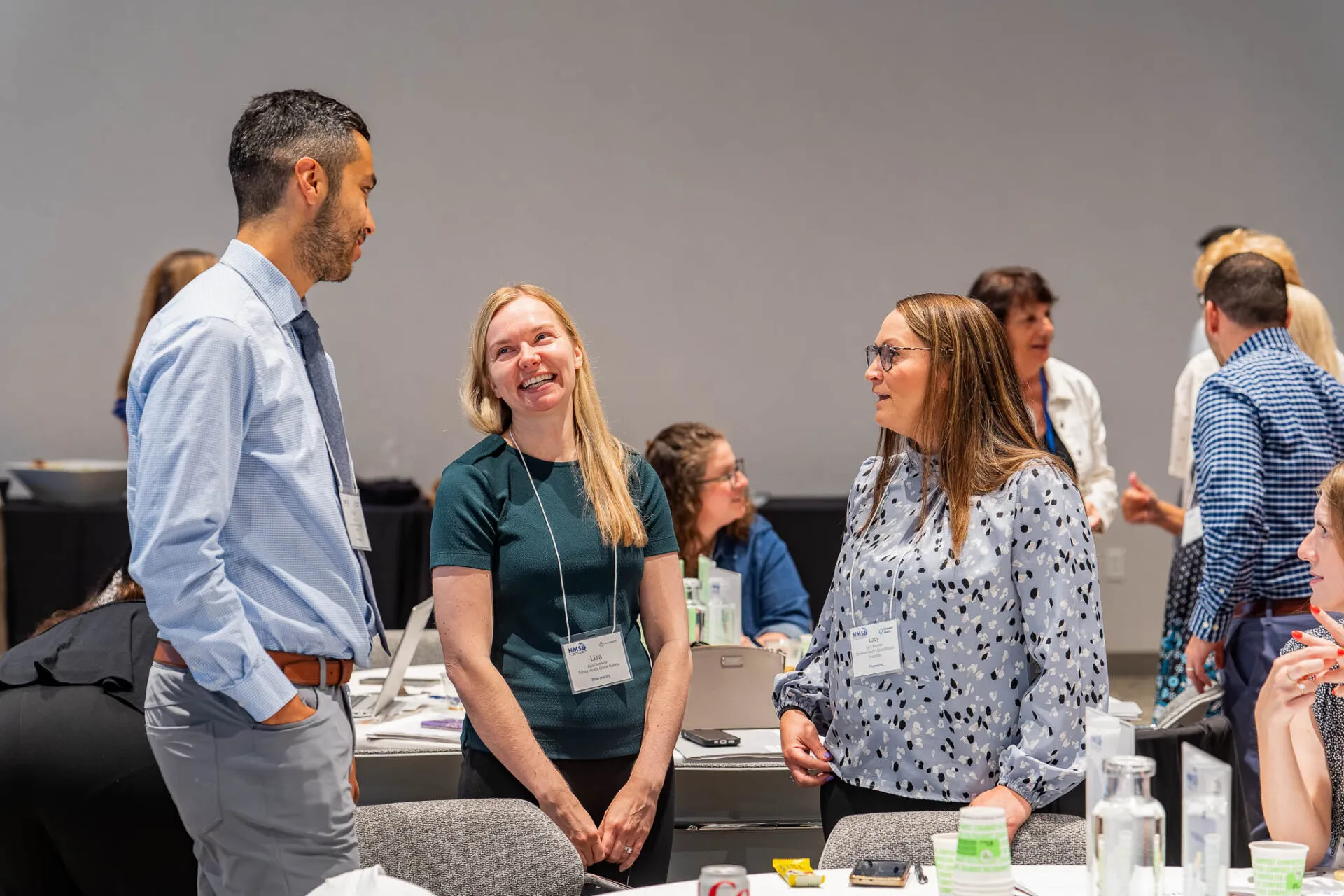 Conference attendees speaking near tables and laughing while they stand.