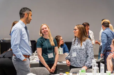 Conference attendees speaking near tables and laughing while they stand.