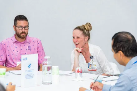 Attendees seated around a conference table during the July HMS meeting, engaged in discussion and collaboration in a professional setting.