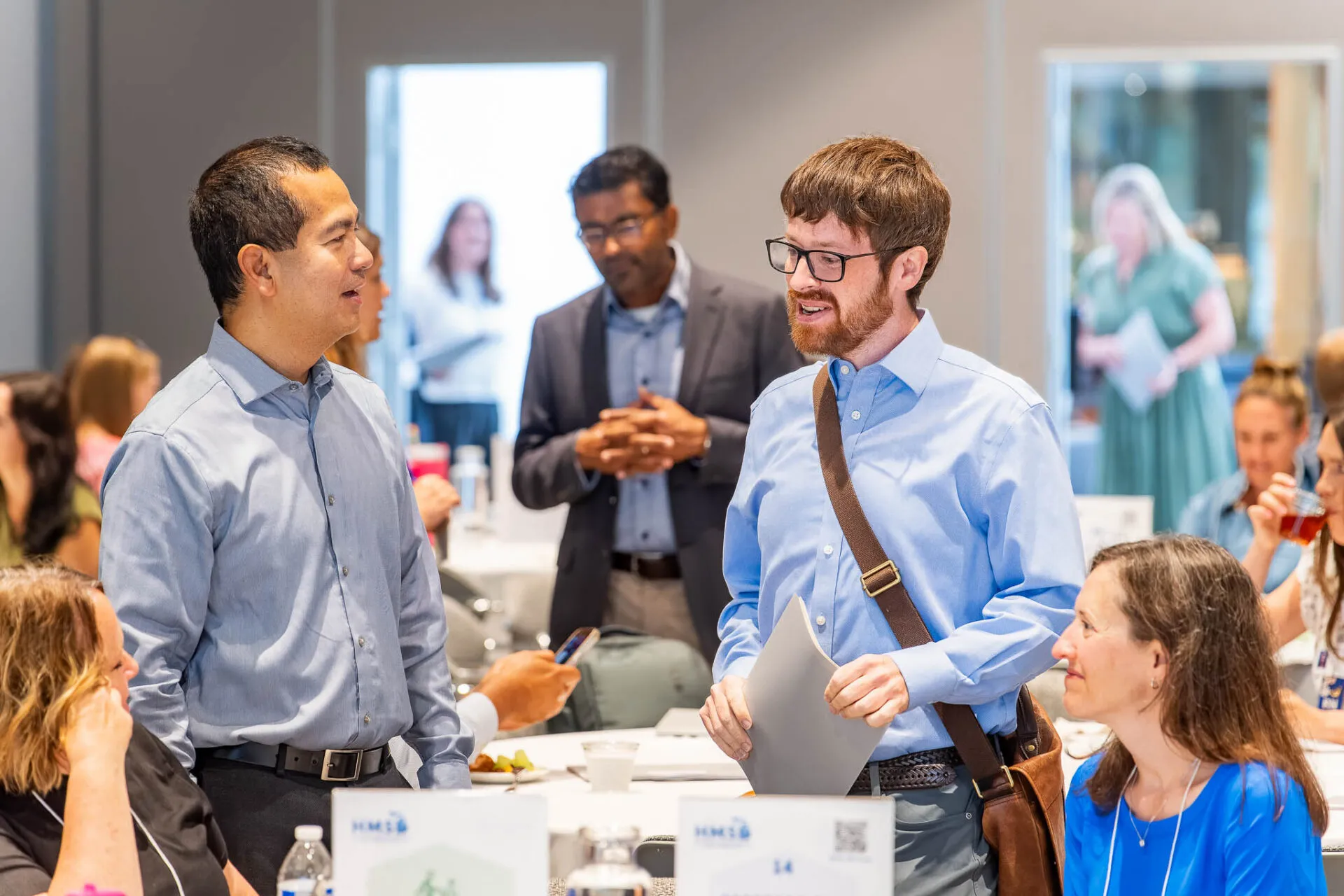 Attendees standing during the July HMS meeting, engaged in discussion and collaboration in a professional setting.