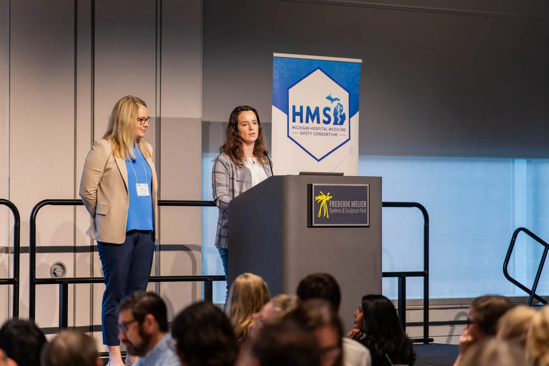 Two woman on a stage speaking near a podium