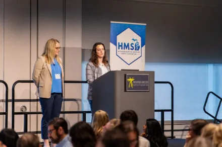 Two woman on a stage speaking near a podium