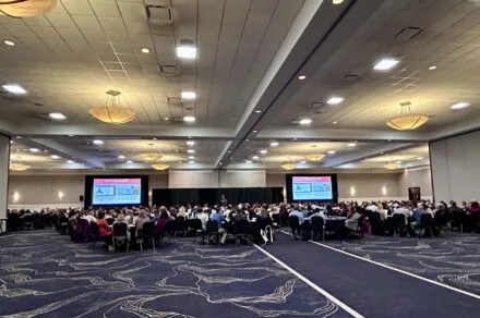 A room with people seated at tables with presentations screens on the left and right
