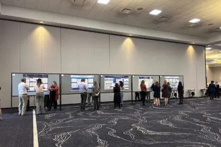 People standing around and discussing QI posters on tackboards.